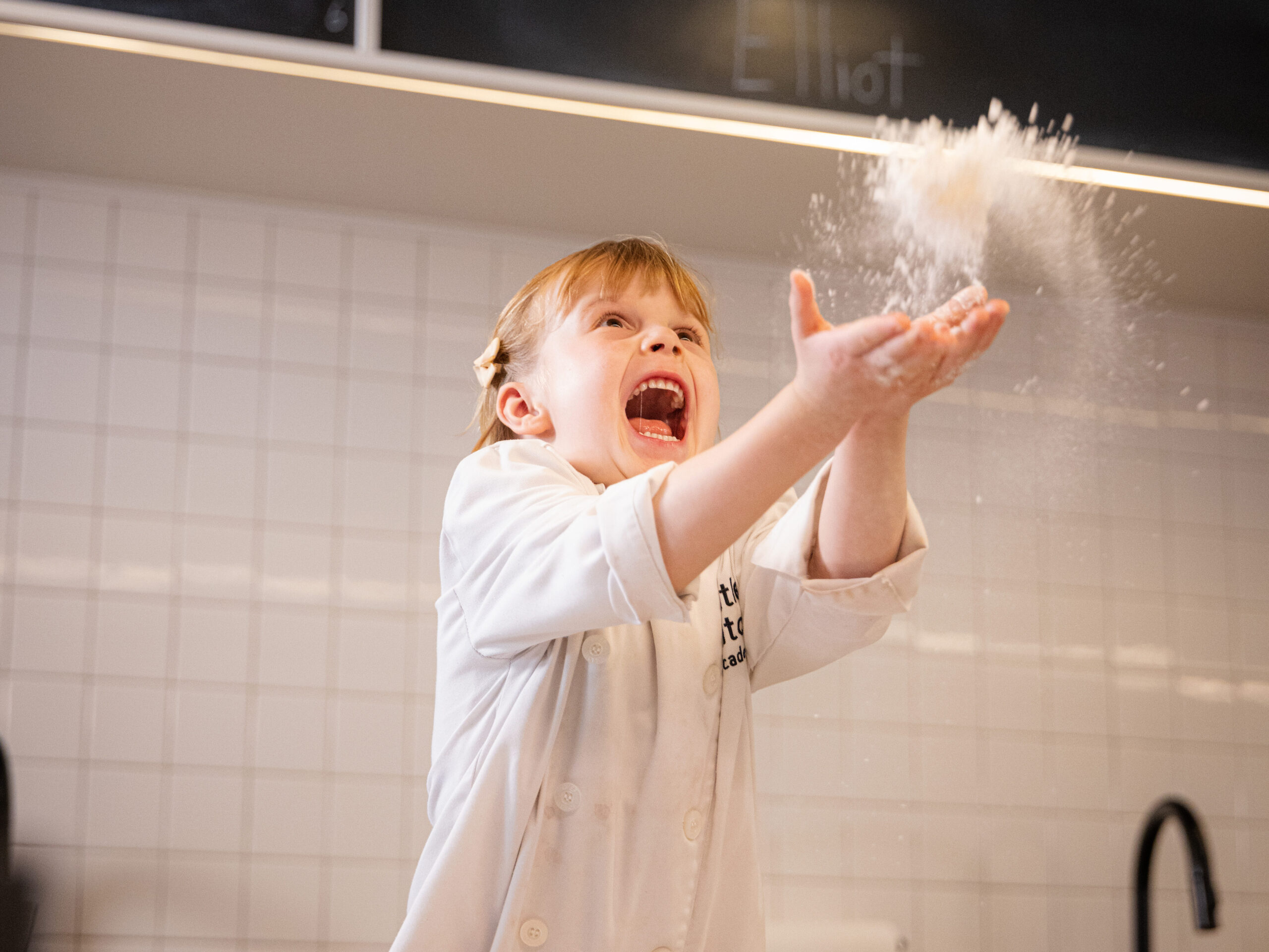 Little Kitchen Academy student joyfully tossing flour in the air.